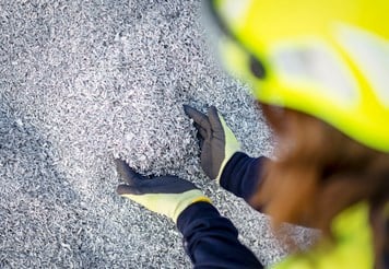 Two hands reaching into an assortment of small pieces of aluminium scrap.